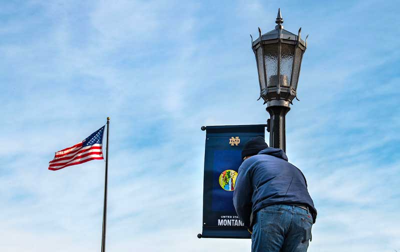 A man installs a banner representing Montana's flag on a lamp post. To the left flies an American flag.