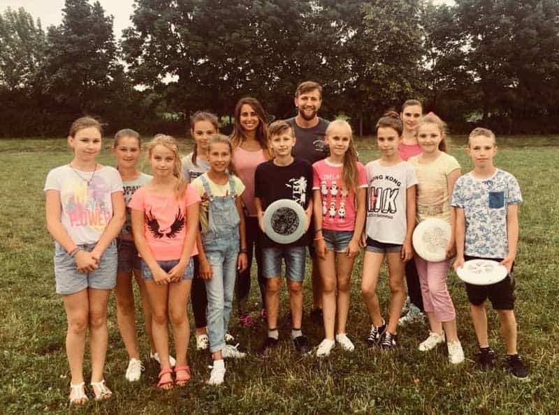 A woman, Mathilda Nassar, poses for a photo in a grassy field with her students, some holding frisbees.