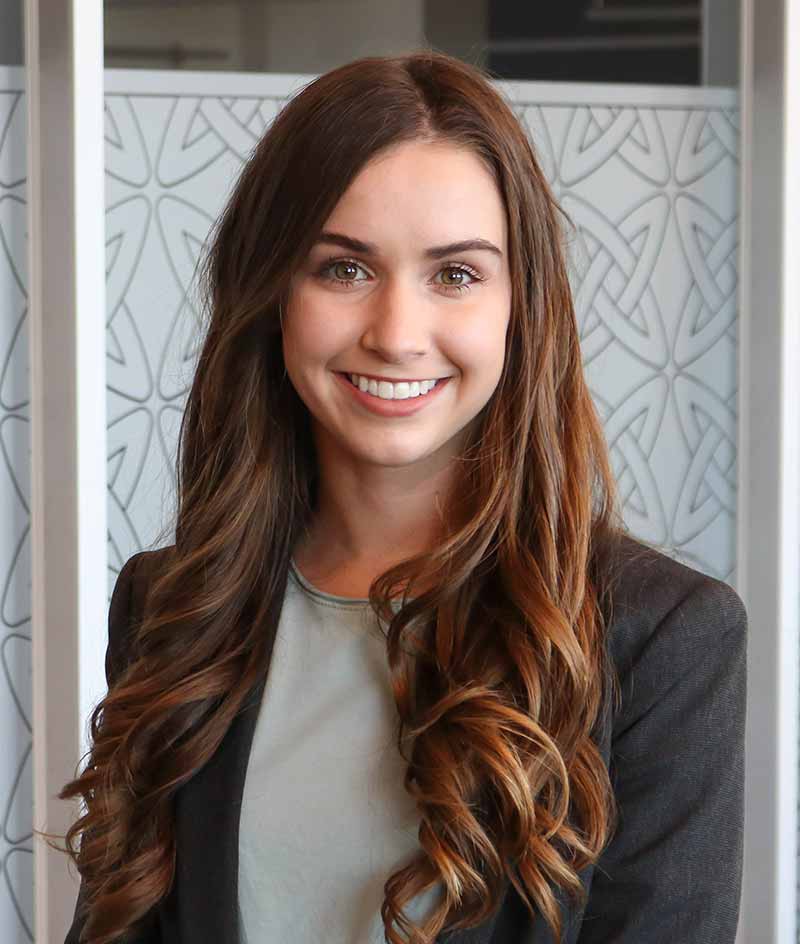 A white female student, wearing a gray jacket and off-green shirt poses for a headshot.