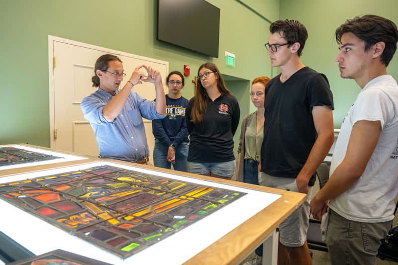 Professor Stephen Hartley explains to students the process of light transfer through glass in front of the mock up panels of Gutenberg on the Press made for the “Protestant Stream of Christianity” window designed by Charles Z. Lawrence for the National Cathedral in Washington DC.