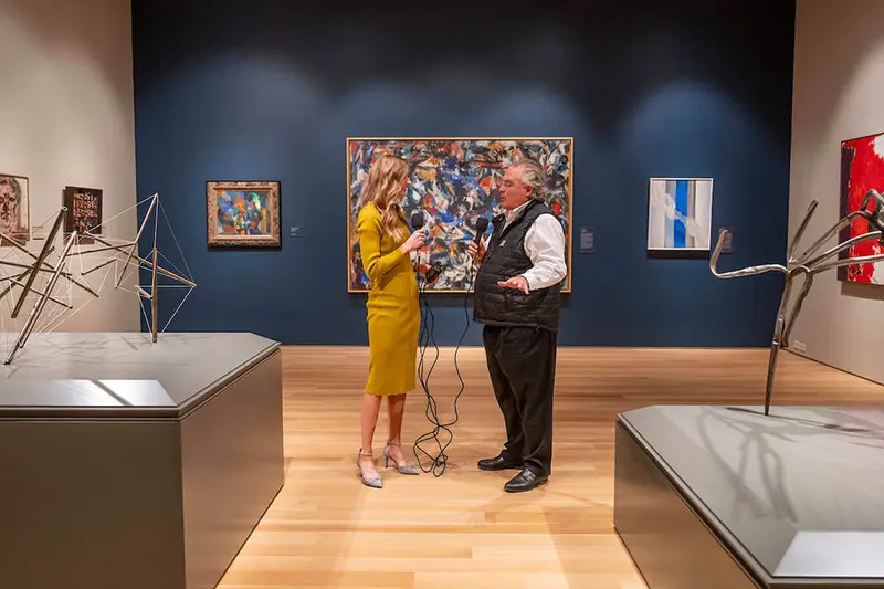 Joe Becherer and Jenna Liberto stand in the art gallery with recording equipment.