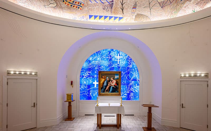 The chapel inside the Raclin Murphy Museum of Art showing an altar with a bright blue stained glass window in the back, and a native american themed mosaic ceiling.