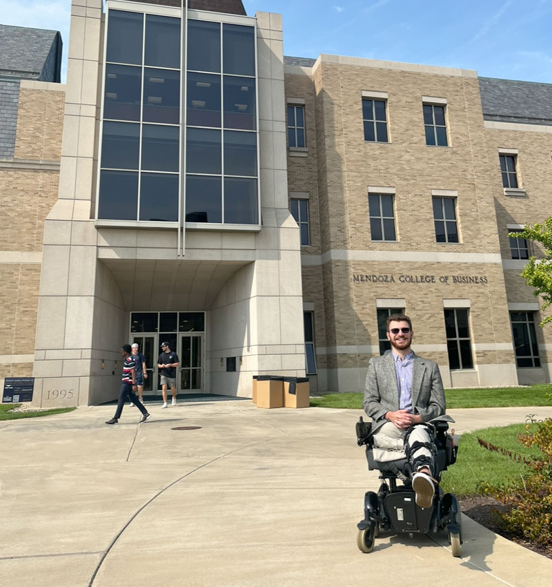 Andrew sits in his wheelchair in front of the Mendoza College of Business