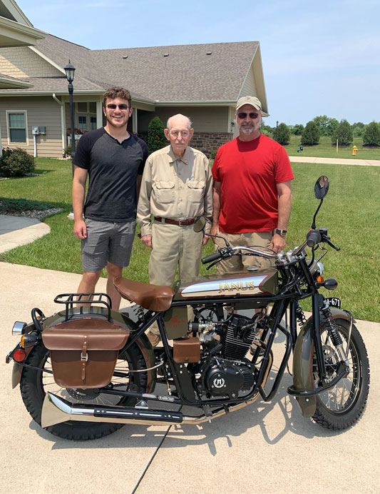 A picture of Andrew before the accident, standing behind a motorcycle with his dad and grandfather.