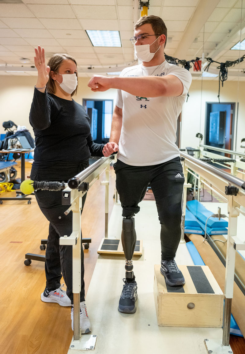 Andrew stands next to his physical therapist doing exercises.