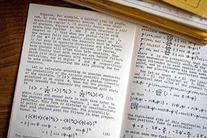 Inside pages of a physics journal, with text and equations, on a wood table.