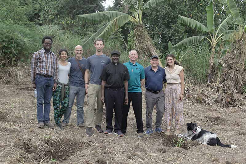 A group of eight people and a dog pose for a group photo in a natural forest.