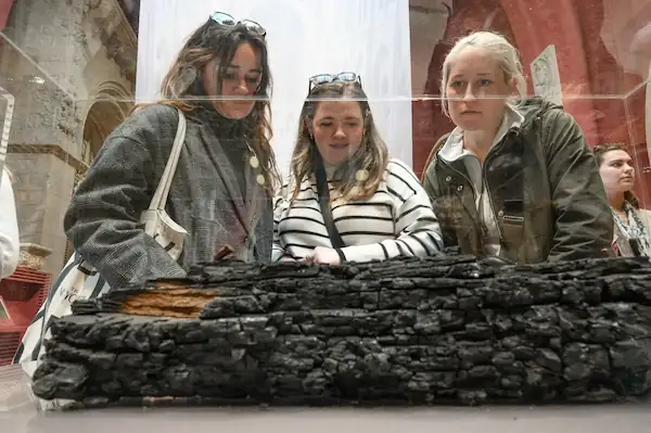 Notre Dame architecture students view a charred beam from the cathedral on display in a glass box.