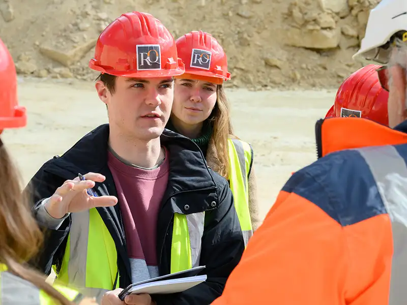 Wearing a hardhat, Notre Dame students speak with the guide while visiting a quarry.