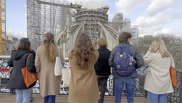 Students facing away looking at the Cathedral of Notre Dame during its restoration after the fire.