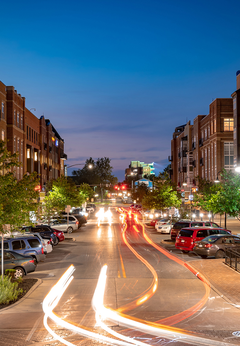 A long exposure photograph of Eddy Street at dusk. Car headlights create light trails as they drive down the road.