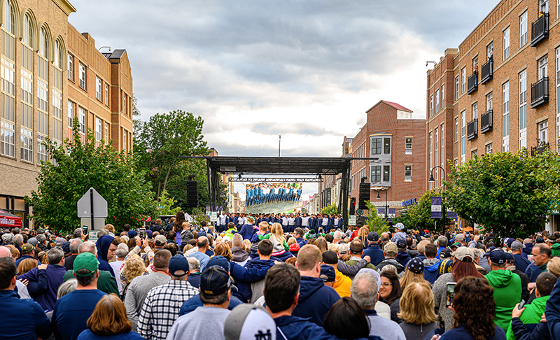 A large group of people gather, many in Notre Dame attire, for a pep rally at Eddy Street Commons.