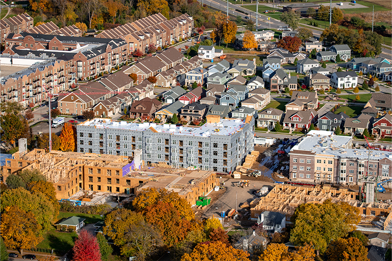 An aerial view of townhomes being built along Eddy Street and adjacent side roads. Three buildings are in various stages of construction, single family homes surround them.