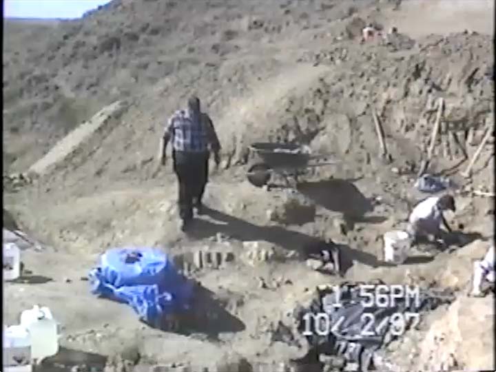 A group people sit on the ground with buckets and tools digging for fossils.