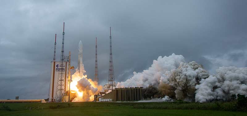 Smoke billows away from a rocketship preparing to take off on a cloudy, gray day.