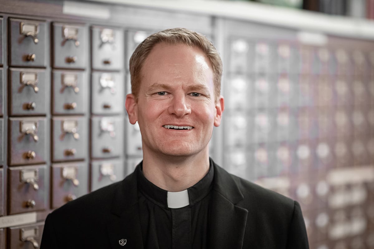 A photo of a white man with red hair in priest’s robe.