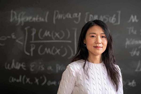 Portrait of a woman professor wearing a white sweater standing in front of a chalkboard with equations written on it.