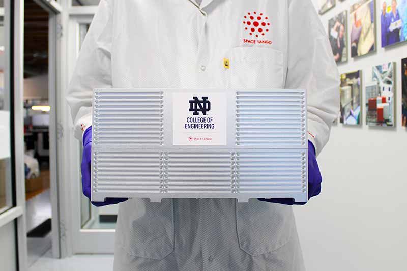 An individual wearing a white lab coat holds a cube. A monogram sticker with College of Engineering on the front of the cube.