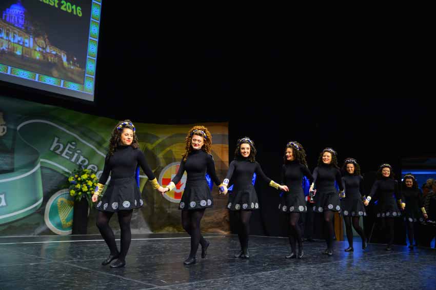 Dancers in black dress walking across the stage holding hands
