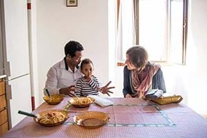 Two adults and a child sit a table with plates of spaghetti.