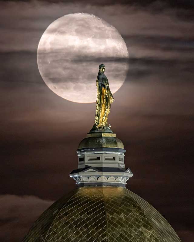 The Moon shines behind thin clouds and Mary ontop the Dome.
