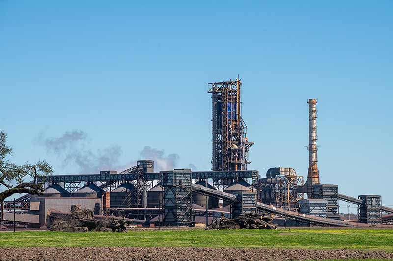 Dark black smoke coming out of an industrail chemical plant against clear blue skies.