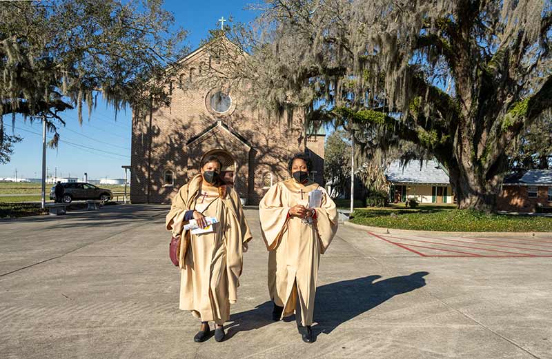 Two women walk outside in front of a brick church.