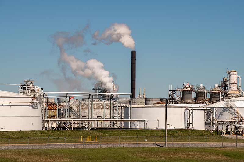 White smoke coming out of an industrail chemical plant against clear blue skies.