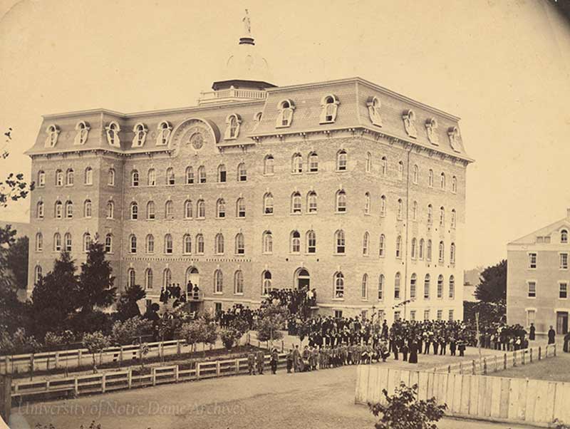 An archival photo of the second Main Building exterior with a crowd of people.