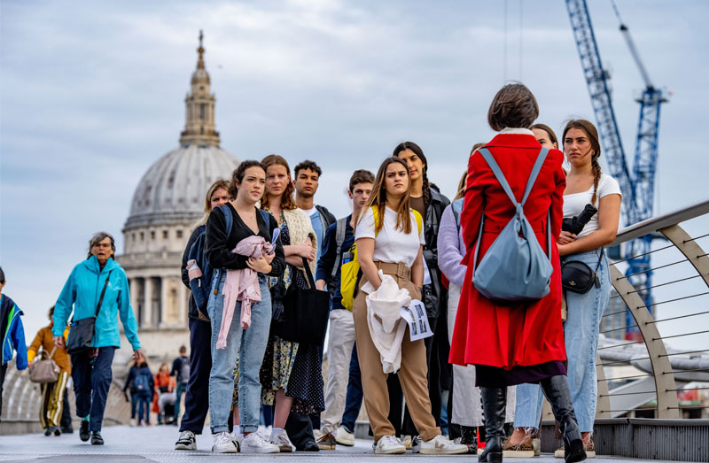 Lois Oliver, in a long red coat, leads a group of students through the streets of London. In the background is St. Paul's Cathedral.