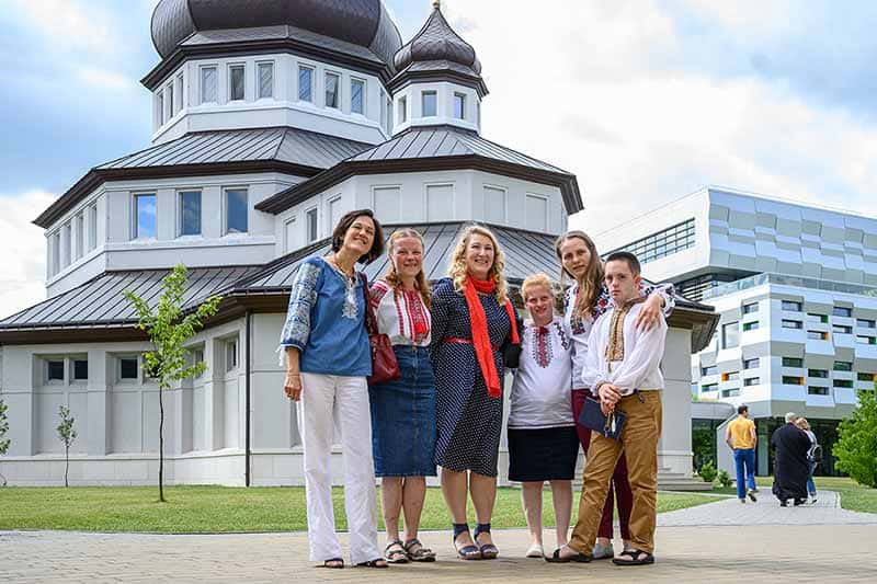 Six people, arms around one another, stand in front of the Church at Ukrainian Catholic University.