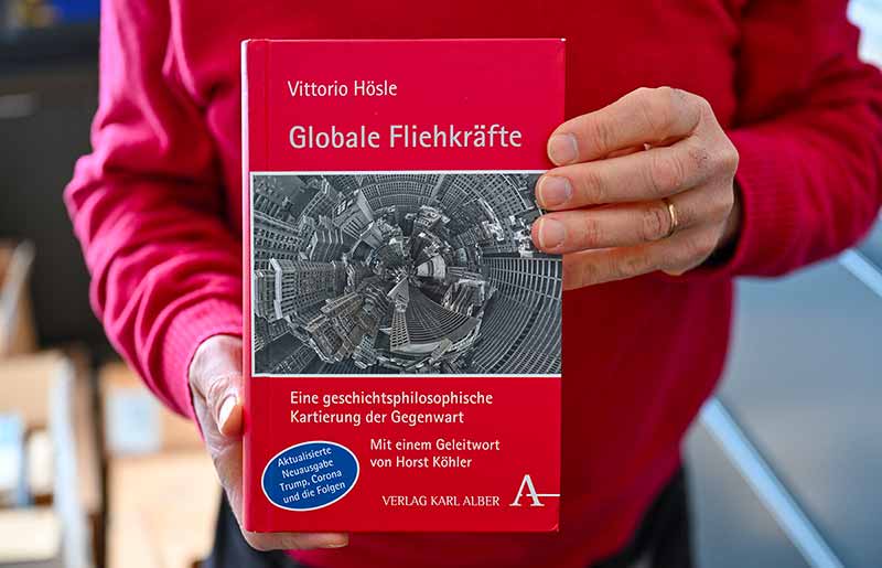 A close up shot of someone holding up a book. The book is in German and has a black and white photo of a distorted view of a skyline.