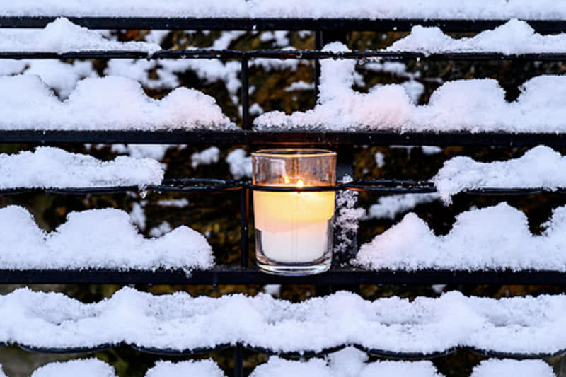 Warmly lit candles on a snow covered rock ledge.