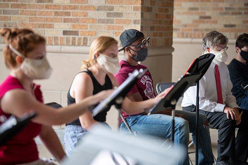 Close-up of students with masks on reading music sheets.