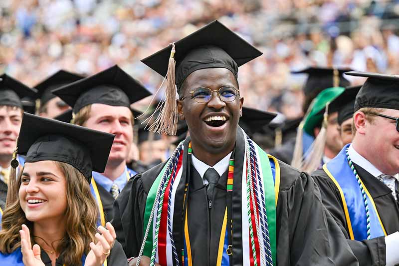 Allan Njomo, a Black man, celebrates and smiles during a Commencement ceremony.