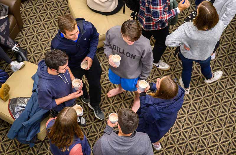 A group of six people stand in a form of a circle, holding cups in their hands, and talking.