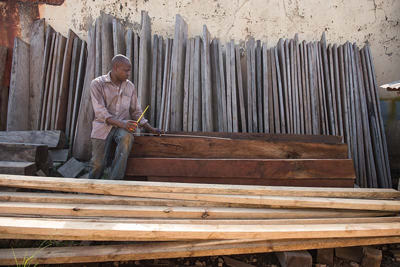 Man from Awaka Furniture sits by stacks of wood.