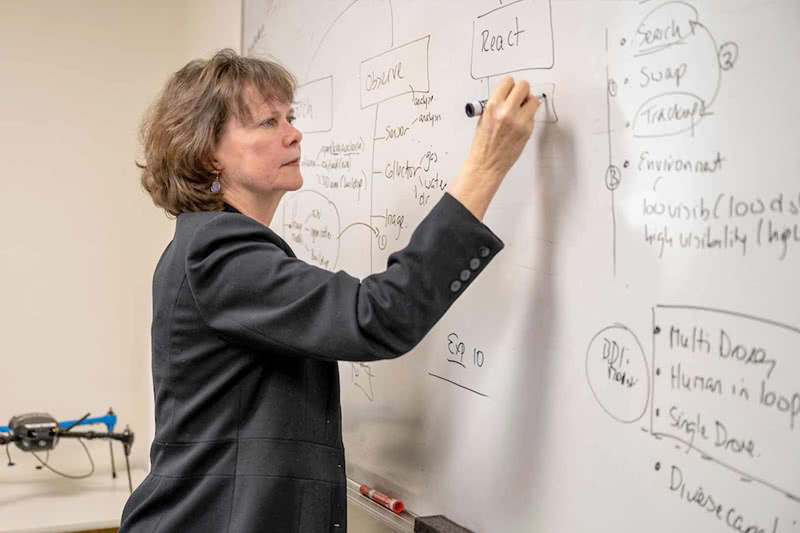 Jane Cleland-Huang standing at a whiteboard writing out concepts for a class.