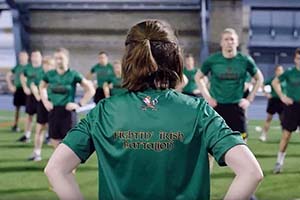 The back of a woman leading ROTC exercises, wearing a green Fighting Irish Battalion shirt.