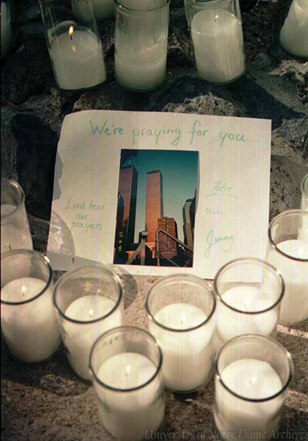 An archive photo of piece of paper with a photo of the World Trade Center and We're praying for you... surrounded by candles at the Grotto.