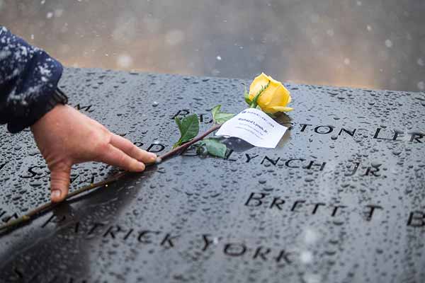 A hand places a yellow rose on the Ground Zero memorial on a snowy day.