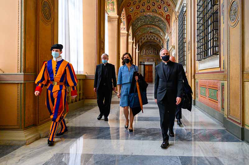A Swiss guard escorts a group of four people, including two priests, down a hallway in the Vatican.