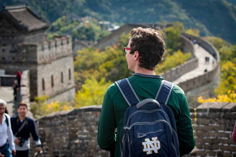 A student wearing a blue Notre Dame backback, looking to the left at the Great Wall of China.